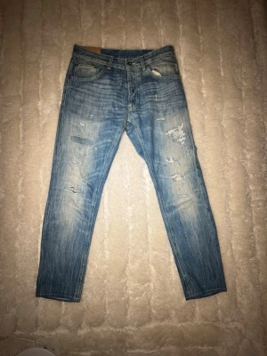 Dondup jeans  - Snygga och trendiga Dondup jeans i blå tvätt med fabriksdistressed detaljer. Premiumdenim med bra passform – perfekt för vardag eller uppklätt casual. ✔️ Märke: Dondup ✔️ Storlek: W30✔️ Passform: Slim / smal (se bilder)✔️ Färg: Blå denim✔️ Midja: Ca 30✔️ Skick: Mycket bra begagnat skick✔️ Detaljer: Slitningar (design), knappgylf, premiumdenim  Slitningarna är design och inte skador. Inga hål som påverkar funktionen, inga fläckar. Jeans i riktigt bra skick.   📦 fraktar snabbt  