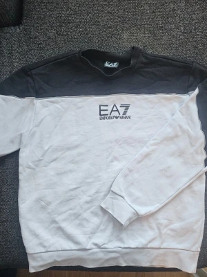 EA7 Emporio Armani svartvit sweatshirt  - Säljer nu min snygga sweatshirt från EA7 Emporio Armani i en stilren svart/vit färgblock-design. Tröjan är i mycket bra skick då den endast är använd 1-2 gånger. Modellen är svår att få tag på. Nypris var ca 1200 kr på rea (Boozt)  Detaljer: Certilogo finns på tvättlappen för att verifiera äkthet (se bild).  Övrigt: Kommer från ett djur- och rökfritt hem.  Tveka inte att ställa frågor 😉