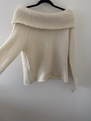 Offshoulder stickad tröja cremevit - Säljer en stickad offshoulder-tröja i cremevit färg. Tröjan har bred ribbad krage som kan bäras nedanför axlarna och långa ärmar. Materialet känns mjukt och mysigt, perfekt för kyliga dagar. Passar dig som gillar en avslappnad men trendig stil.