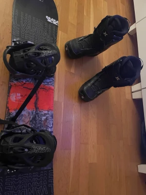 Snowboard K2 Vandal med boots - Säljer en K2 Vandal snowboard med svart och orange design samt matchande svarta bindningar. Medföljer ett par svarta snowboardboots med vita detaljer. Perfekt för dig som vill ha ett komplett snowboardpaket till vinterns äventyr.