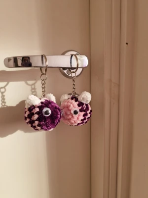 Söta fluffiga nyckelringar djurmotiv/ bumblebee couple keychains  - Två handgjorda nyckelringar med fluffiga bollar i lila och rosa, dekorerade med vita öron och rörliga ögon. Perfekta att hänga på väskan eller nyckelknippan för en gullig touch. Tillverkade av mjukt garn och metallkedja. Bumblebee couple keychains 