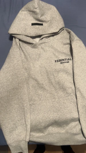  Essentials Fear of God hoodie - Snygg grå hoodie från Fear of God Essentials med svart logga på bröstet och stor print på ryggen. fint skick utan hål eller fläckar. Oversized passform.