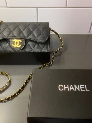 Svart Chanel  - Snygg svart axelväska från Chanel i quiltat läder med klassiskt guldigt CC-spänne framtill. Väskan har en lång kedjerem i guld och svart läder, perfekt för att bära över axeln. Ikonisk design som lyfter varje outfit. Säljas så snabbt som möjligt + pris kan diskuteras !!