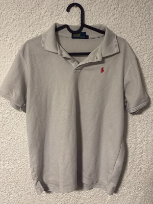 Vit pikétröja från Polo Ralph Lauren - Klassisk vit pikétröja från Polo Ralph Lauren med korta ärmar och krage. Tröjan har den ikoniska röda logobroderingen på bröstet och är tillverkad i mjuk bomull. Perfekt till jeans eller shorts för en clean och stilren look. Storlek L men passar M bättre. Kan gå ner i pris vid snabb affär!