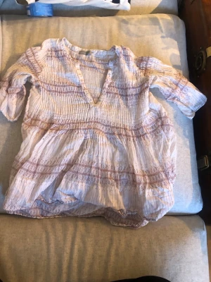 Bohemisk blus med mönster - Luftig boho-inspirerad blus i vitt med rosa och beige mönster. Blusen har v-ringning, smockad överdel och trekvartsärm. Tillverkad i ett tunt, skrynkligt tyg som ger en avslappnad känsla.