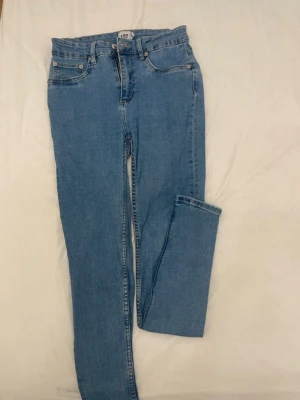 Ljusblå skinny jeans från 457 - Säljer ett par ljusblå skinny jeans från 457 med klassisk femficksdesign och normalhög midja. Jeansen har dragkedjegylf och silverfärgade nitar. Perfekta till en avslappnad och trendig look.
