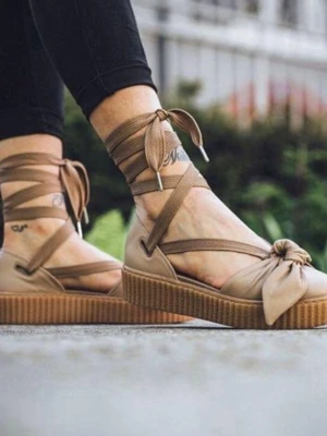 Puma Fenty By Rihabnna - Snygga beige sandaler med bred platåsula och dekorativ rosett framtill. Sandalerna har långa knytband som lindas runt ankeln för en trendig look. Tillverkade i textil och syntetmaterial, perfekta för sommarens outfits. Har använt dom endast 2 ggr och säljer dom pga dom passar inte min fot 