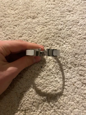 Silverfärgat armband med vita detaljer - Snyggt armband i silverfärgad metall med vita detaljer på sidorna. Armbandet har en stilren och modern design med ett smidigt lås. Perfekt accessoar för att lyfta din outfit med en clean look.