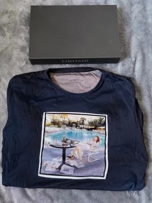  Limitato t-shirt  - Snygg mörkblå t-shirt från Limitato med ett stort färgglatt tryck framtill som visar en avslappnad poolscen. Klassisk rund hals och korta ärmar. Perfekt för dig som vill ha en unik och trendig look.