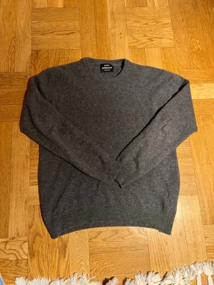 Grå stickad tröja från Mads Nørgaard - Mysig grå stickad tröja från Mads Nørgaard Copenhagen. Klassisk rund halsringning och långa ärmar. Tröjan är i mjukt material och har ribbade muddar vid ärmslut och nederkant. Perfekt för lager på lager under kyliga dagar.