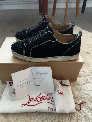 Svarta Louboutins med nitar - Snygga svarta sneakers från Christian Louboutin med klassiska röda sulor och coola svarta nitar på tån. Unika vita detaljer. Skorna är i mycket bra skick med inga defekter. Skorna är nydligen inlämnade hos en skomakare. Kan skicka fler bilder. Kommer med box och kvitto mm. 