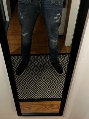 Mörkblå slitna slim fit jeans - Snygga mörkblå slim fit jeans med slitningar och distressed detaljer på låren och knäna. Klassisk femficksmodell med låg midja och smal passform. Perfekta för en trendig och avslappnad look.