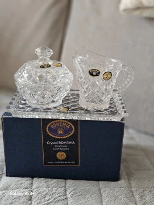 Kristallset från Bohemia - Säljer ett elegant kristallset från Bohemia, tillverkat i Tjeckien. Setet består av en sockerskål med lock, en liten kanna och ett rektangulärt fat, allt i genomskinlig slipad kristall med klassiskt rutmönster. Perfekt för att lyfta fikastunden.