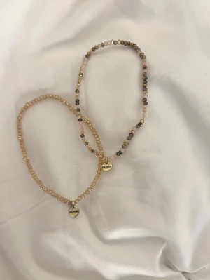 Armband Pilgrim - Två jättesöta armband med glaspärlor i beige och guld , båda har en liten runt metallbricka av pilgrim loggan.