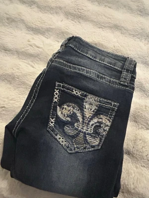 Jeans med snygga bakfickor! - Snygga mörkblå jeans från Gina Tricot med kontrastsömmar och unik broderad ficka bak med silverfärgat mönster. Klassisk femficksmodell och låg midja. Perfekta för dig som vill sticka ut med coola detaljer och bekväm passform. Aldrig andvända!