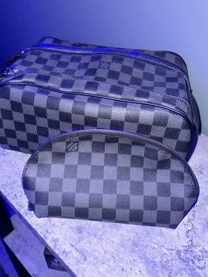 Louis Vuitton rutiga necessärer - Två snygga necessärer från Louis Vuitton i klassiskt svart och grått damier-mönster. Tillverkade i tåligt canvasmaterial med detaljer i svart läder och silverfärgade dragkedjor. Perfekta för att organisera dina essentials när du är på språng.