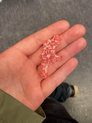 Sour patch kid som ser ut som en gubbe som drar i slangen - Unikt rött gelégodis täckt med socker, format i en ovanlig figur. Godiset är mjukt och har en tydlig sockrig yta som ger en syrlig smak. Perfekt för dig som gillar roliga former på godis.
