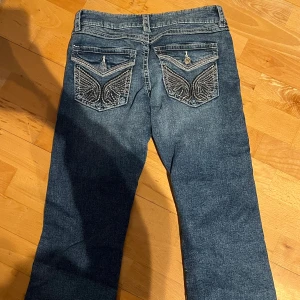 Blå bootcut jeans med broderade fickor - Snygga blå lågmidjade bootcut jeans med coola broderade detaljer och knappar på bakfickorna. Endast testade och säljer för att jag har för många jeans 