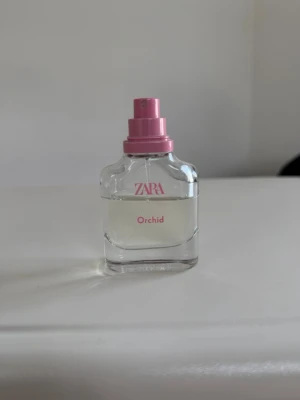 Zara Orchid Eau de Parfum - ZARA Orchid parfym i en genomskinlig glasflaska med rosa spraymunstycke. Flaskan har en enkel, modern design med rosa text. Doften är fräsch och feminin, perfekt för dig som gillar blommiga toner. Smidig storlek att ha med i väskan.