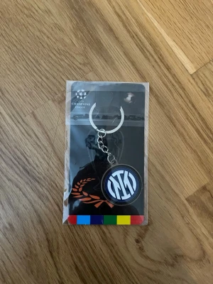 Inter Milan nyckelring Champions League - Säljer en snygg nyckelring med Inter Milans logga i svart, blått och vitt. Nyckelringen är officiellt licensierad för Champions League och har en rund form med metallkedja. Perfekt accessoar för fotbollsfans!