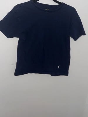 Mörkblå t-shirt från Polo Ralph Lauren - Klassisk mörkblå t-shirt från Polo Ralph Lauren med rund hals och korta ärmar. Tillverkad i 100% bomull och har den ikoniska lilla loggan broderad framtill. Perfekt basic-plagg för en clean och stilren look.