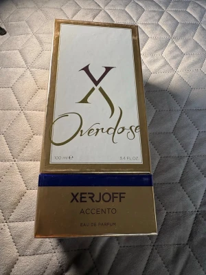 Xerjoff Accento Overdose EdP 100ml - Lyxig parfym från Xerjoff, Accento Overdose, i en elegant guldig och vit förpackning med blå detalj. Flaskan rymmer 100 ml Eau de Parfum och utstrålar exklusivitet och modern stil. Perfekt för dig som vill sticka ut med en unik doft.
