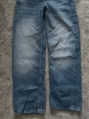 Blå raka jeans - Ett par blå jeans med rak passform och lätt tvättad look. Jeansen har klassisk femficksdesign och är tillverkade i denim. Perfekta för en avslappnad och trendig stil.
