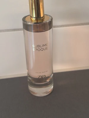 ZARA Sublime Epoque Eau de Parfum - ZARA Sublime Epoque Eau de Parfum i en elegant cylinderformad glasflaska med guldigt lock. Flaskan är transparent med subtil rosa ton och stilren text. Perfekt för dig som gillar moderna och fräscha dofter.