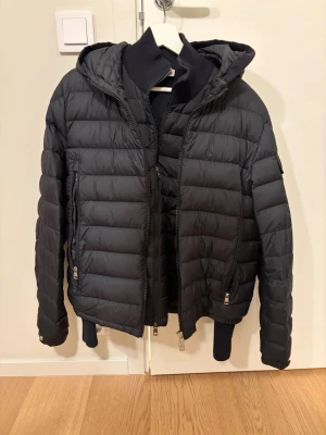 Svart pufferjacka med huva Moncler - Snygg svart pufferjacka från Moncler med huva och dragkedja framtill. Jackan har två sidofickor med dragkedja och ribbade muddar vid ärmslut och nederkant. Perfekt för kalla dagar och riktigt skön att bära. Använd ett par gånger ny pris 15.000kr (kvitto finns) Mitt Pris 5500k. Passar både M/L