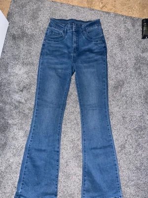 Blå bootcut jeans med hög midja - Snygga blå bootcut jeans med hög midja och klassiska fem fickor. Jeansen har en lätt utsvängd passform nedtill och är gjorda i ett mjukt denimtyg. Perfekta för en trendig och avslappnad look.