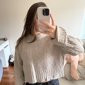 Beige ribbstickad croppad tröja - Snygg beige ribbstickad tröja med croppad passform och långa ärmar. Tröjan har en högre rund halsringning och är gjord i ett mjukt, tjockare material som ger en avslappnad look.