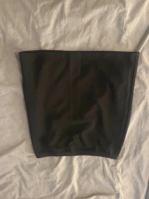 Svart bandeau tubtopp - En stilren svart bandeau tubtopp med tight passform. Toppen är axelbandslös och har en enkel, minimalistisk design utan synliga detaljer eller mönster. Perfekt att styla med höga jeans eller kjol för en clean look.