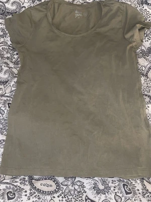 Olivgrön basic t-shirt - En enkel olivgrön t-shirt med rund hals och korta ärmar. Tillverkad i mjuk bomull som känns skön mot huden. Perfekt till jeans eller shorts för en avslappnad look. Djur finns i hemmet, tvättas innan leverans.💕