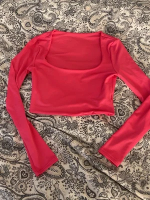 Rosa croppad långärmad topp - Trendig rosa croppad topp med långa ärmar och rundad, djup urringning fram. Tillverkad i ett tunt, stretchigt syntetmaterial som ger en smickrande passform. Perfekt att styla med höga jeans eller kjol. Djur finns i hemmet, tvättas innan leverans.💘