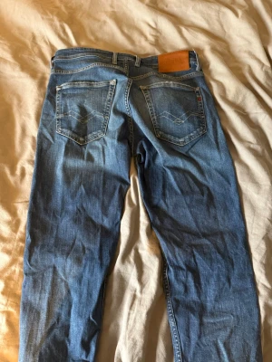 Blå jeans från Replay grover - Säljer ett par klassiska blå jeans från Replay med raka ben och fem fickor. Jeansen har snygga slitningar framtill och kontrastsömmar. Tillverkade i denim med en skön passform och detaljerade bakfickor.