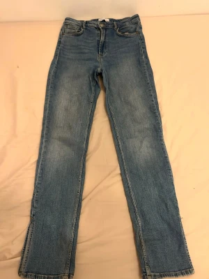 Blå raka jeans med rå kant - Säljer ett par ljusblå jeans med rak passform och råa, fransiga benslut. Jeansen har klassisk femficksdesign och är gjorda i denim med lätt tvättad look. Perfekta för en avslappnad och trendig stil.