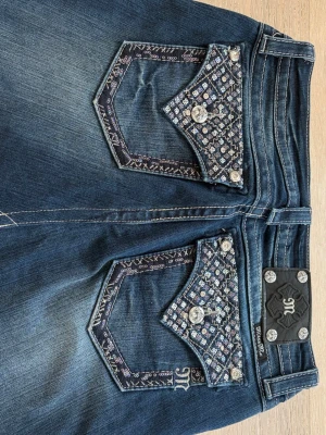 Miss me fjol  - Snygg mörkblå jeanskjol med dekorativa bakfickor med mönster och knappar. Klassisk femficksmodell med diamantknappar. Perfekt för dig som gillar en cool och trendig stil.
