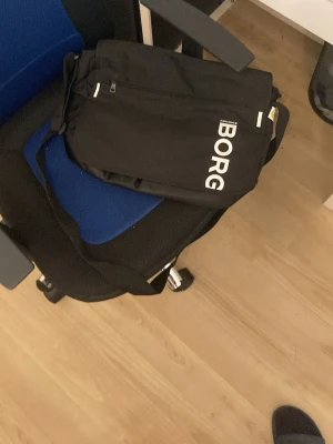 Svart axelväska från Björn Borg - Snygg svart axelväska från Björn Borg med justerbar axelrem och tydlig logga i vitt på framsidan. Väskan har flera fack, dragkedja och praktisk design i slitstarkt tygmaterial. Perfekt för att bära med sig det viktigaste till skolan eller stan.