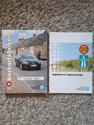 Körkortsboken + Vägmärken & Vägmarkeringar, 2013 - Två kursböcker för körkort: Körkortsboken (utgåva 23) med färgfoto på bil och hus samt Vägmärken & vägmarkeringar med omslag i blått och grönt. Perfekt för dig som pluggar till körkort. Böckerna är tryckta på papper och har mjuka pärmar. Skick: 6/10