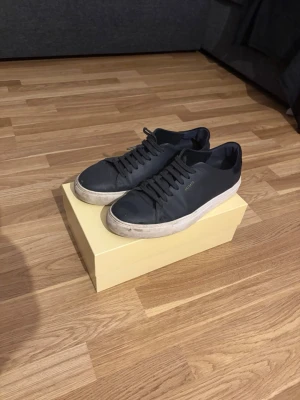 Svarta sneakers från Axel Arigato - Snygga svarta sneakers från Axel Arigato med klassisk design och vita sulor. Skorna är gjorda i läder och har diskret logotyp på sidan. Perfekta för dig som gillar stilrena och trendiga skor med en clean look.