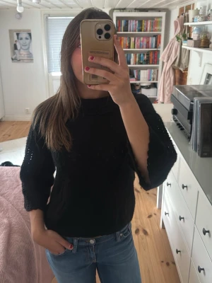 Svart stickad tröja med vida ärmar - Säljer en svart stickad tröja med trekvartsvida ärmar och lös passform. Tröjan har ett diskret hålmönster längs ärmarna och en mjuk, bekväm känsla. Perfekt att styla med jeans eller kjol för en chill look.
