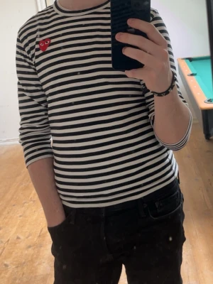 Randig långärmad tröja Comme des Garçons - Säljer en svartvit randig långärmad topp från Comme des Garçons Play med det ikoniska röda hjärtat på bröstet. Klassisk rund halsringning och slim passform. Perfekt för dig som gillar stilrena och trendiga plagg. Bra skick och inget täcken på användning. 