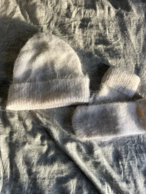 Vit fluffig mössa i mohairmix - Säljer en vit, mjuk och fluffig mössa i mohairmix. Mössan har en klassisk form med uppvikt kant och känns riktigt cozy och varm. Perfekt för kalla dagar när du vill ha en stilren och enkel look.