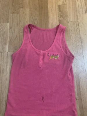 Rosa ribbad linnetopp med leopard - Snygg rosa ribbad linnetopp med knappar framtill och ett broderat leopardmotiv på bröstet. Perfekt för dig som gillar djurmönster och vill ha en bekväm och trendig topp till sommaren.