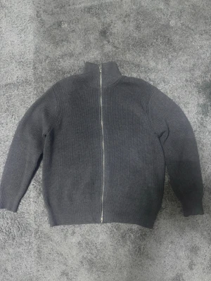 Maison margiela full zip  - Maison Margiela full zip i mörkgrå färg. Enkel och stilren design med dragkedja och hög hals. 