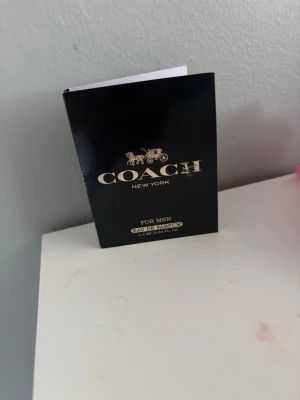 Coach New York Eau de Parfum för män - Coach New York Eau de Parfum för män i en elegant svart förpackning med guldfärgad text och logga. Doften är maskulin och exklusiv, perfekt för dig som vill ha en modern och stilren parfym. Förpackningen innehåller 1,2 ml.