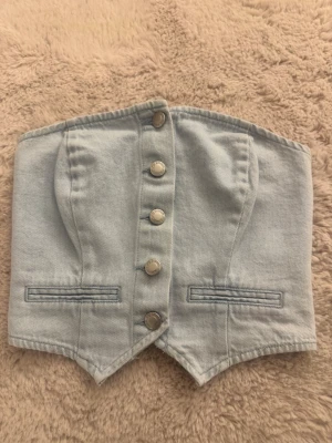 Ljusblå denim korsett - Säljer en snygg ljusblå korsettopp i denim från New yorker (FB Sister). Toppen har markerade sömmar, dekorativa fickor och silverfärgade knappar framtill. Passar till både jeans och kjol!