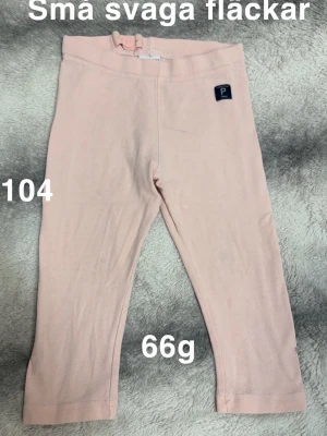 Ljusrosa leggings - Säljer ett par ljusrosa leggings med resår i midjan och en liten dekorativ lapp framtill. Perfekta till vardags för en avslappnad look.🌸 Ej hellånga. Små svaga fläckar. Storlek 104