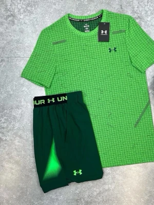  Under Armour sommar sett  - Snyggt grönt träningsset från Under Armour med t-shirt och shorts. T-shirten har ett rutigt mönster och logga på bröstet, medan shortsen har elastisk midja med logga och matchande grön detalj. Perfekt för gym eller löpning.