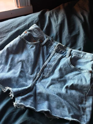 Levi's ljusblå jeansshorts - Ljusblå jeansshorts från Levi's med råa, fransiga benslut och klassisk femficksdesign. Shortsen har medel midja och är gjorda i slitstark bomull. Perfekta för varma dagar och en avslappnad stil.
